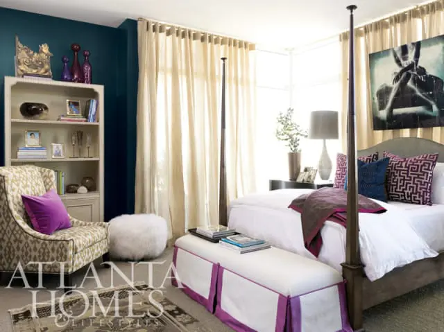 Bedroom with teal accent wall, four-poster bed, patterned armchair, and large abstract artwork above the bed.