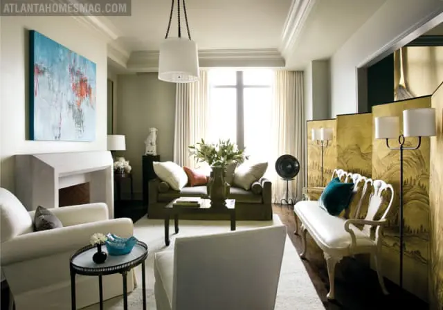 Living room with a modern fireplace, abstract art, neutral-toned sofas, a white bench, and a gold folding screen with landscape art.