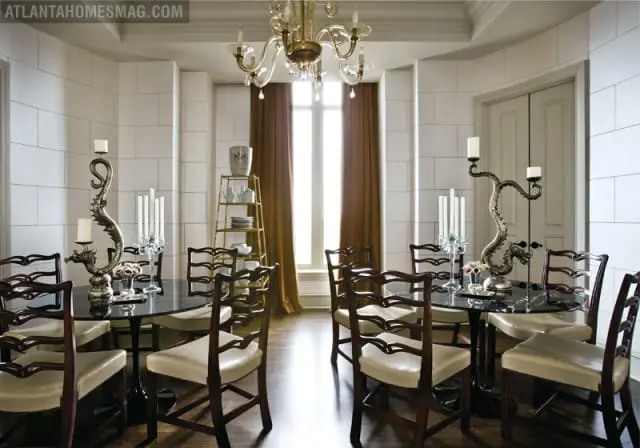 Formal dining room with white tiled walls, dark marble-topped tables, and upholstered chairs. A gold étagère and ornate candelabras are visible.