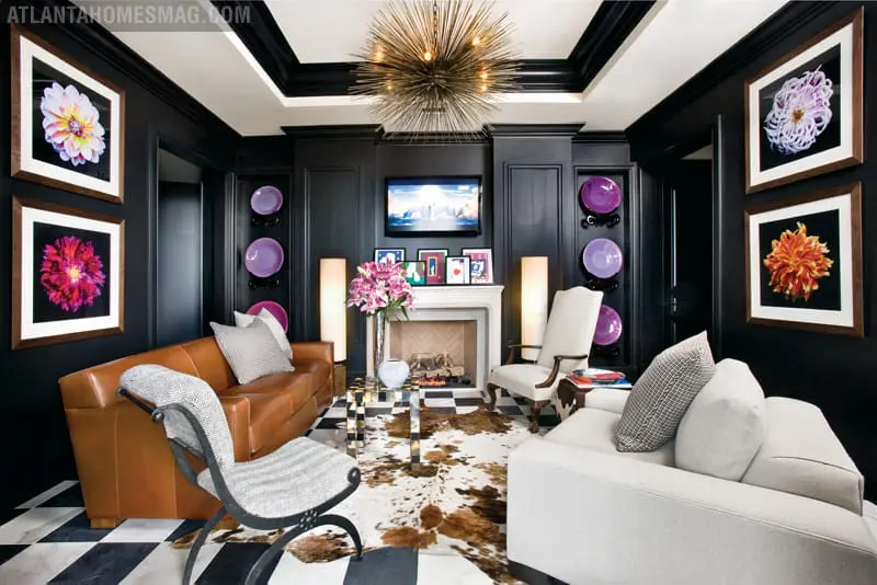 Living room with black paneled walls, featuring a brown leather sofa, white sofa, fireplace, and framed floral art.