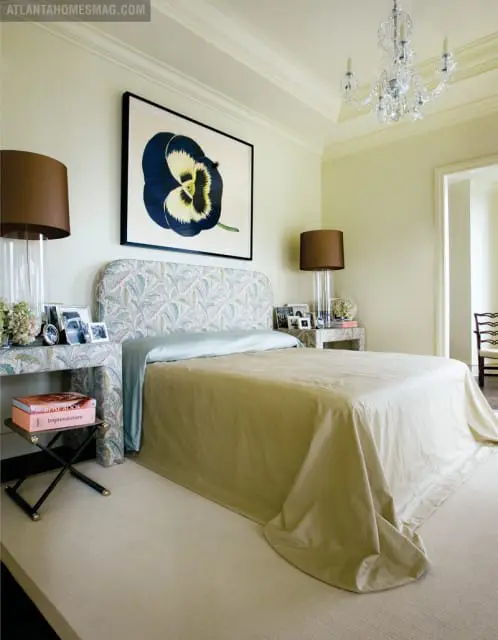 Bedroom with a large framed botanical print of a pansy above a bed with a patterned headboard and a light beige coverlet.