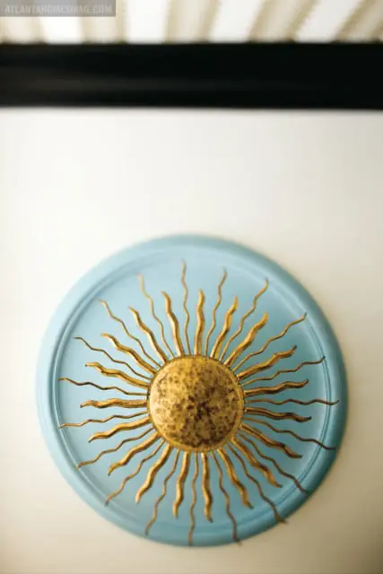 Gold sunburst wall art with textured center mounted on a light blue circular plaque.