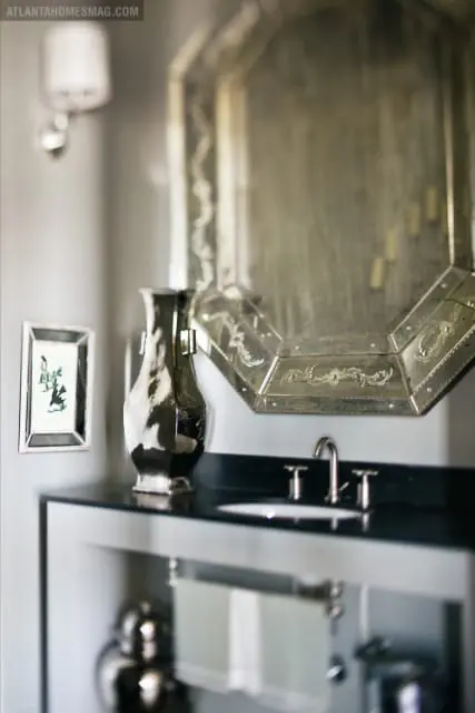 Gray bathroom with black granite vanity, octagonal mirror with ornate frame, and silver vase.