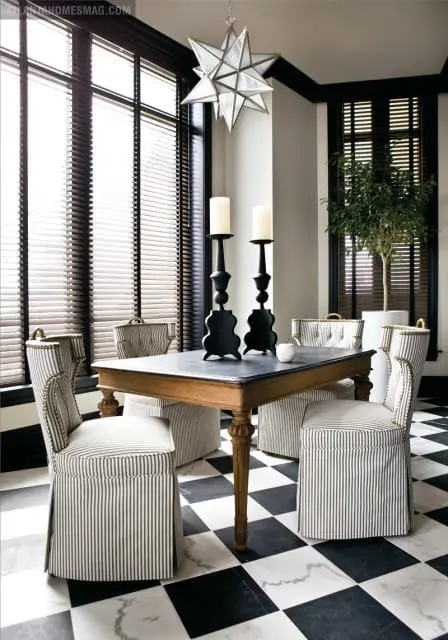 Dining room with black and white checkered marble floor, striped upholstered chairs, a dark-topped wooden table with ornate legs, and a starburst chandelier.