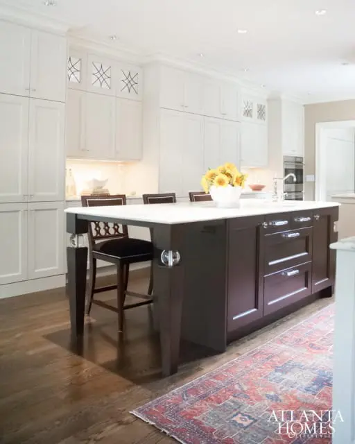 White kitchen with custom cabinetry, dark wood island with marble countertop, and a vintage rug.