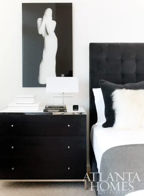 Bedroom with a black tufted headboard, black dresser with silver hardware, and a large black and white artwork of a draped figure.