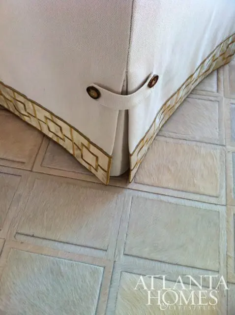 Close-up of upholstered furniture with decorative gold trim and brown buttons, resting on a rug made of light-colored hide tiles.