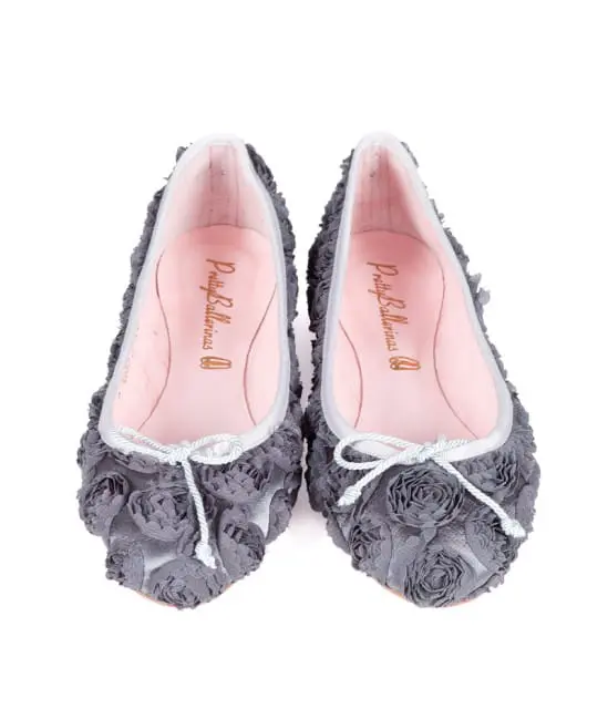 Pair of grey ballet flats with fabric rose embellishments and small white bows on the toes. The insoles are pink with "Pretty Ballerinas" printed in script.