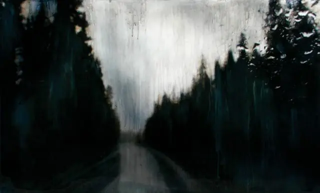 Dark, silhouetted trees line a wet, empty road under a bright, overcast sky with streaks of rain.