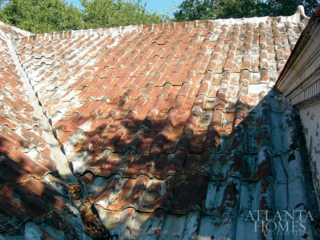 Close-up of weathered, red clay roof tiles with patches of white and dark discoloration, showing signs of age and wear.