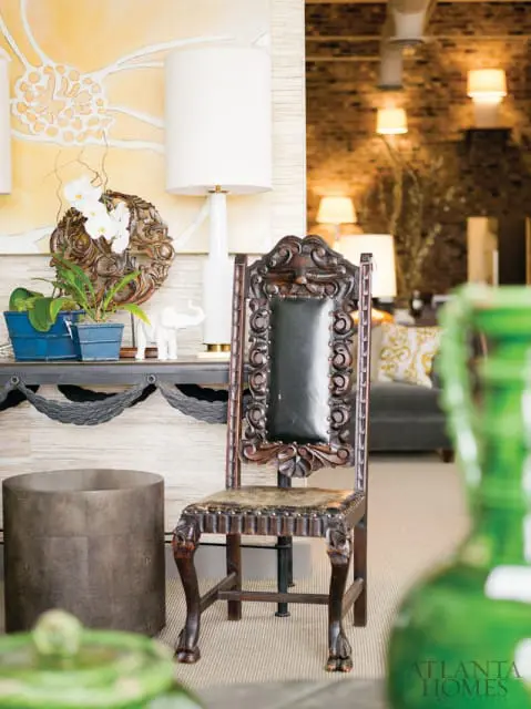 Ornate dark wood chair with black leather upholstery and carved details, placed next to a cylindrical metal side table.