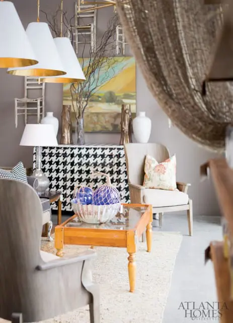Living room with a houndstooth cabinet, a wooden armchair with a floral pillow, and a glass-top coffee table with blue glass spheres in a decorative bowl.
