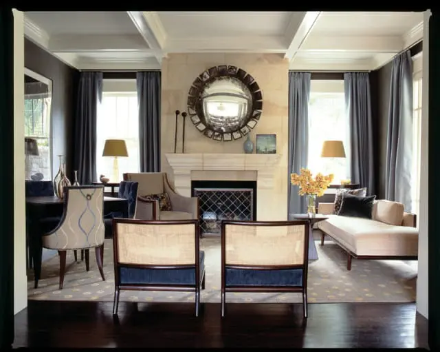 Living room with coffered ceiling, stone fireplace, and cane-backed chairs. Dominant colors are gray, beige, and dark wood.