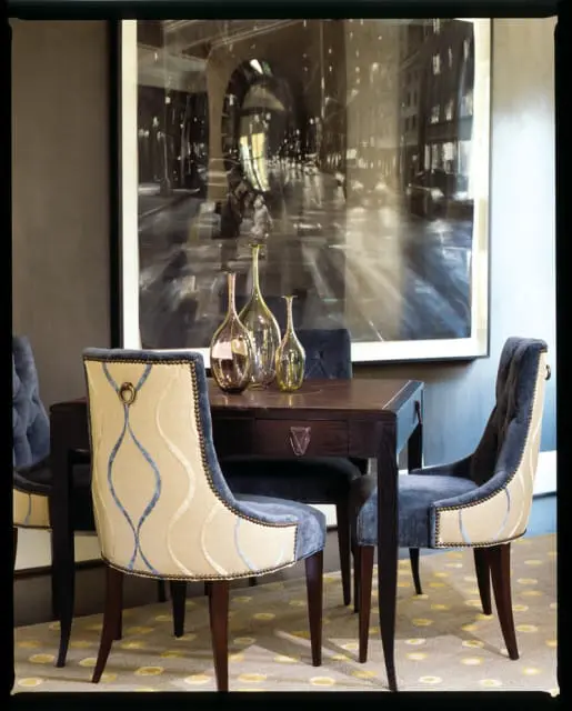 Dining room with dark wood table and chairs upholstered in blue velvet and cream fabric with blue wavy pattern. Large black and white cityscape artwork hangs on the wall.