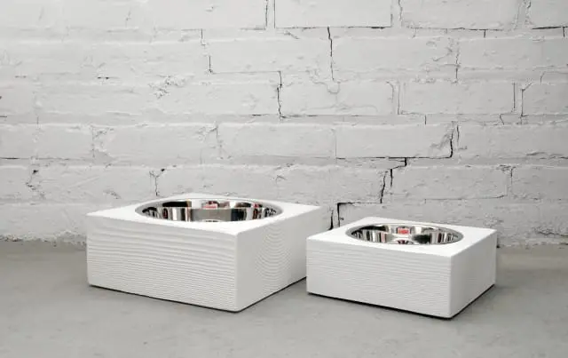 Two white wooden pet bowls with stainless steel inserts against a white brick wall.