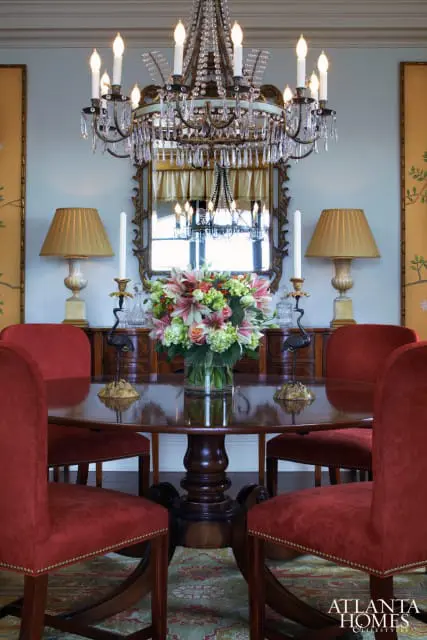Dining room with a round mahogany table, plush red chairs, a crystal chandelier, and a large mirror above a wooden buffet.