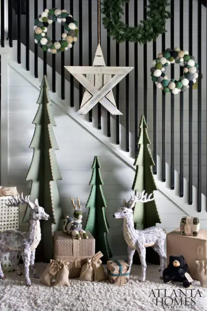 White staircase with black banisters decorated for Christmas with wreaths, a wooden star, cardboard trees, and reindeer figures.