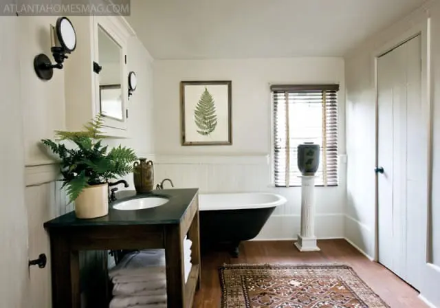 Cream bathroom with a black clawfoot tub, dark wood vanity with a white sink, wainscoting, and a framed fern print above the tub.