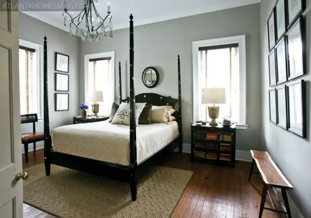 Bedroom with a black four-poster bed, neutral bedding, and gray walls. A crystal chandelier hangs above the bed, and framed artwork adorns the wall.