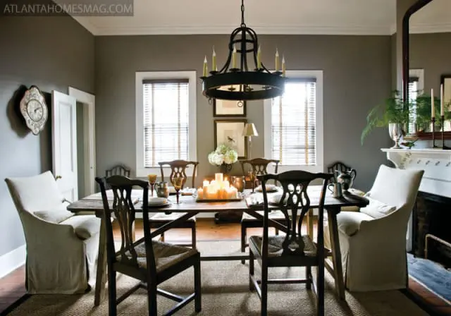 Dining room with dark wood table set for a meal, surrounded by dark wood chairs and slipcovered armchairs. A large ornate chandelier hangs overhead.