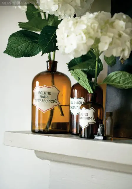Amber glass apothecary bottles with white labels containing Latin text, holding white hydrangeas, displayed on a white shelf.