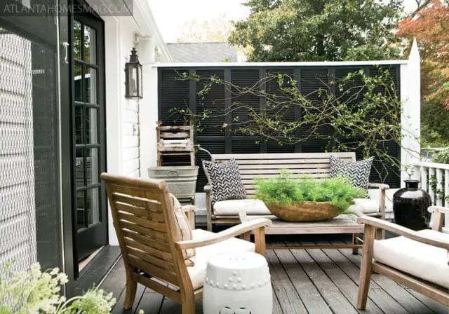 Wooden porch with slatted bench and chairs, black louvered screen, and decorative lantern.