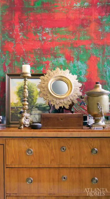 Wooden dresser topped with a brass samovar, a sunburst mirror, a framed landscape painting, and a gold candlestick with a white candle.