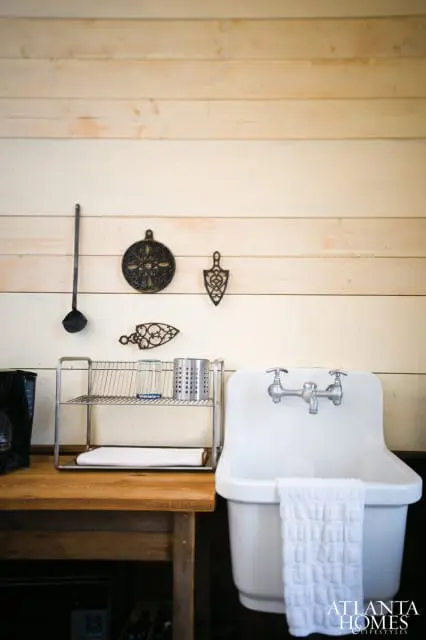 White farmhouse sink with chrome faucet and white waffle-weave towel hanging. Wooden countertop with metal dish rack holding glass and utensil holder.