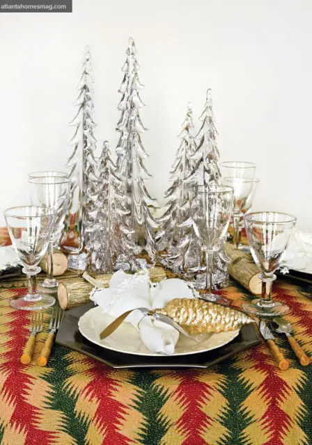 Table setting with clear glass Christmas trees, gold pinecone ornaments, and a colorful patterned tablecloth.
