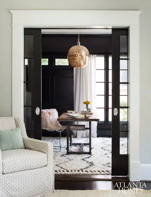 A home office with black paneled walls, a wooden desk, and a large ornate pendant light. A patterned armchair is in the foreground.