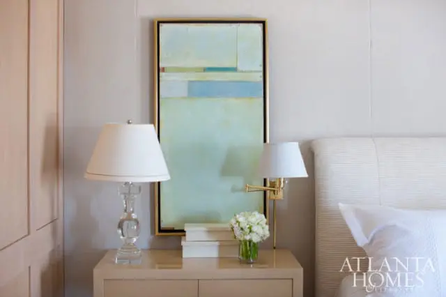 Bedroom with a light neutral palette, featuring a glass lamp, abstract art, and a striped headboard.