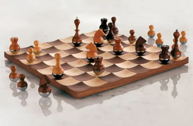 Wooden chess pieces with silver bases on a wavy wood chessboard with alternating light and dark squares.