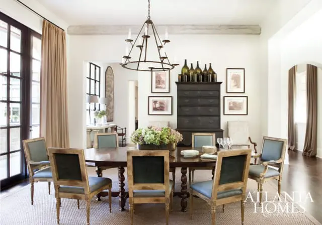 Dining room with oval wooden table, upholstered chairs in blue and green, dark wood chest, and a metal chandelier.