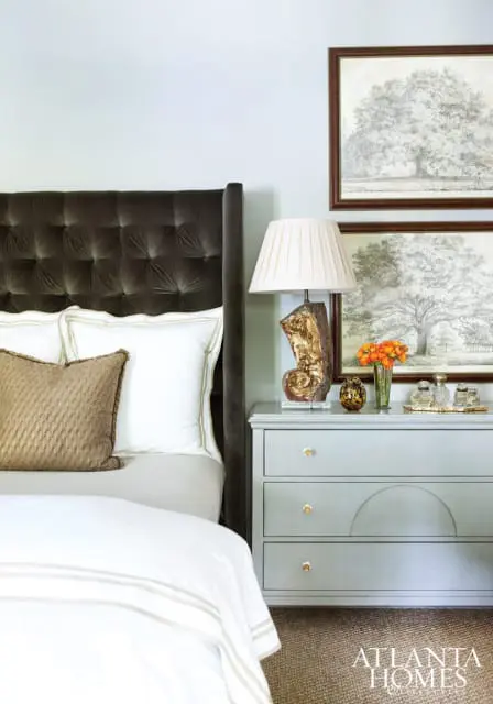 Bedroom with a dark gray tufted headboard, light blue walls, and a light gray dresser. Artwork of trees hangs above the dresser.