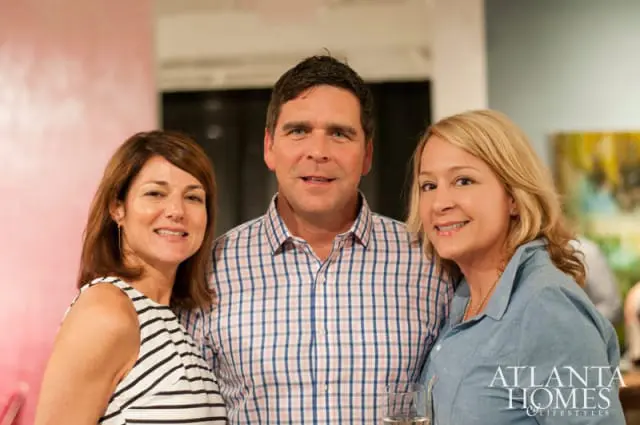 Three people pose for a photo, two women and one man. The woman on the left wears a black and white striped top. The man in the center wears a pink and blue plaid shirt. The woman on the right wears a blue button-down shirt. The Atlanta Homes & Lifestyles logo is visible in the lower right corner.