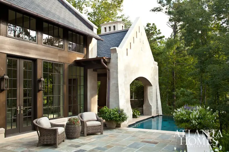 Tuscan-style home exterior with dark-framed windows, arched loggia, plunge pool, and stone patio. Wicker seating is arranged on the patio.