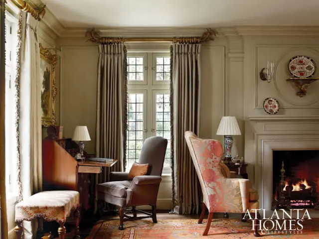 Traditional living room with a fireplace, wingback chairs, antique writing desk, and ornate curtains.