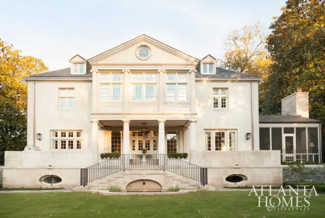 Large stone mansion with a central portico supported by columns, multiple windows, and a screened-in porch.