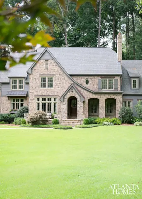 Brick house with gray roof, arched entryway, multiple windows, and manicured lawn. Atlanta Homes & Lifestyles logo in the lower right corner.