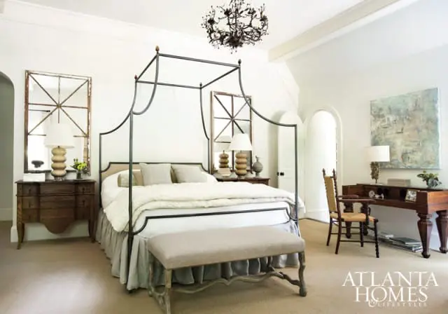 Bedroom with a black metal canopy bed, neutral bedding, a linen bench, and a dark wood dresser with a large framed mirror above it.