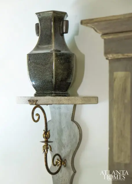 Close-up of a dark speckled ceramic vase on a stone shelf with an ornate gold sconce below.