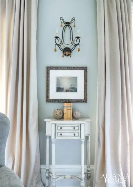 Pale blue walls with a vintage-style sconce, framed artwork of a ship, and a narrow white console table topped with books and decorative spheres.