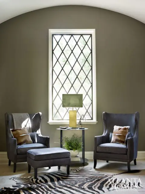 Two dark gray wingback chairs flank a tall diamond-paned window. A zebra print rug covers the floor in front of the chairs.