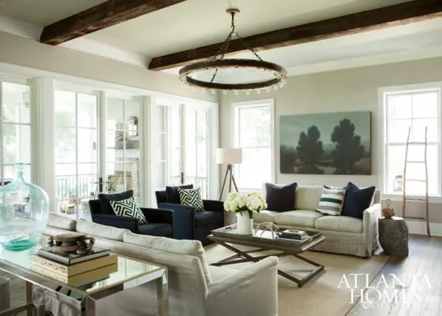 Living room with neutral sofas, navy armchairs with geometric pillows, exposed wood beams, and a large circular chandelier.