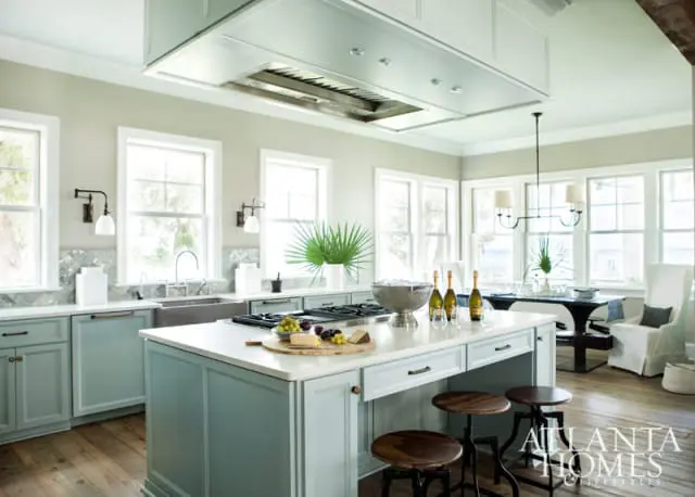 Light blue kitchen island with white countertop, gas range, and seating for three. Stainless steel range hood above.