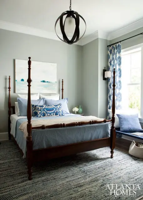 Bedroom with a dark wood four-poster bed, blue and white patterned bedding, a landscape painting, and a geometric pendant light.