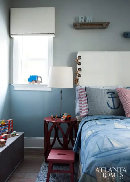 Blue and gray boy's bedroom with a white headboard, sailboat bedding, and wooden toy truck on the windowsill.