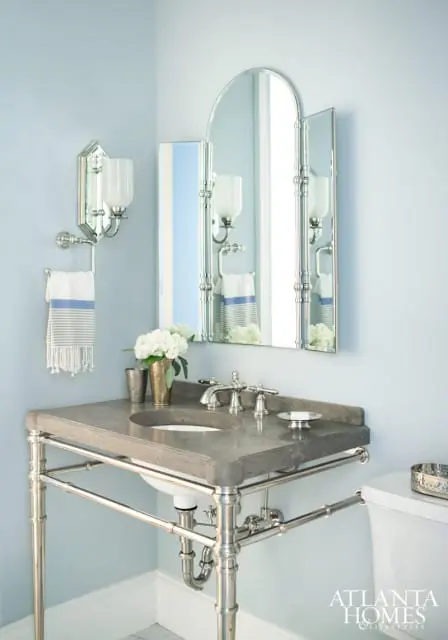 Powder room with light blue walls, a gray concrete vanity with a chrome stand, a triptych mirror, and a striped hand towel.