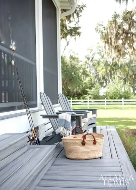 Screened porch with gray Adirondack chairs, fishing rods, woven basket, and a blue and white striped throw blanket.