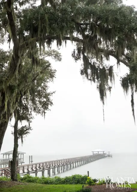 Long wooden pier extending into a misty body of water, framed by trees draped in Spanish moss. A small gazebo is visible on the left side of the pier.